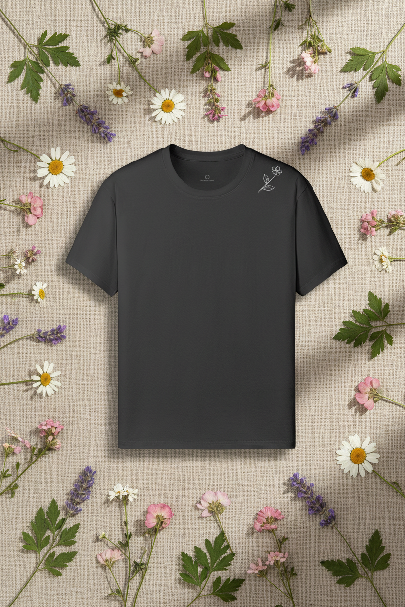 Charcoal grey Wildflower Tee with wildflower line-art laid on natural linen with pressed wildflowers