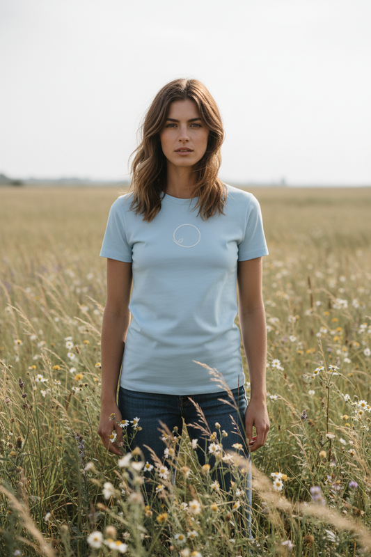 Woman wearing light blue Orbit Slim tee with orbit line-art on front, standing among wild grasses and wildflowers