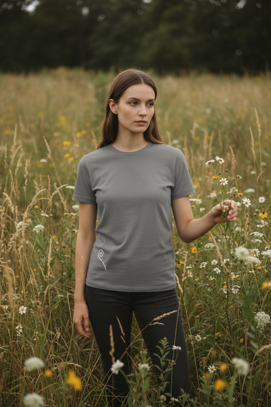 Person wearing grey Fiddlehead Slim tee with fiddlehead fern line-art, standing among wild grasses